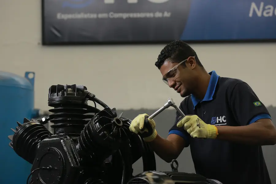 Técnico da HC Compressores realizando manutenção em compressor industrial de pistão dentro de oficina técnica equipada.