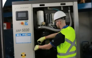 Técnico realizando manutenção em compressor de parafuso industrial, verificando componentes internos e sistema de ar comprimido.
