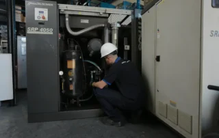 Técnico realizando inspeção em compressor de parafuso industrial para identificar falhas e perda de pressão no sistema de ar comprimido.