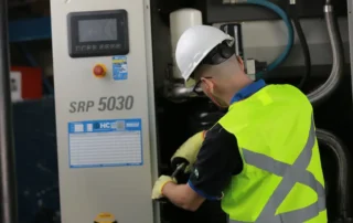 Técnico realizando manutenção em compressor de parafuso industrial, ajustando componentes internos do sistema de ar comprimido.