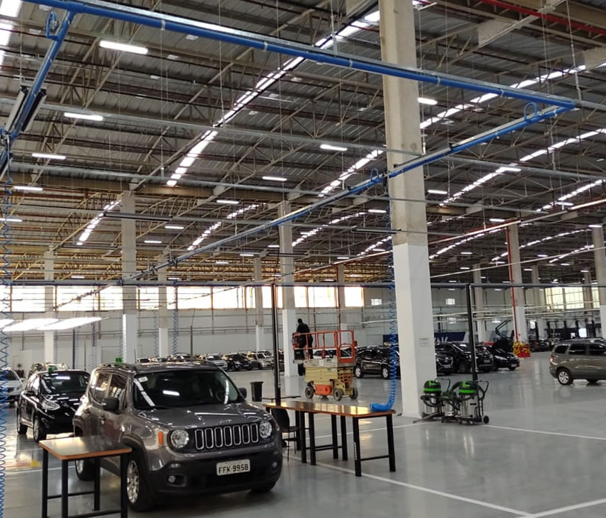Rede de ar comprimido em tubulação azul instalada no teto de uma fábrica automotiva, com descidas espiraladas até as bancadas e pontos de consumo na linha de produção.