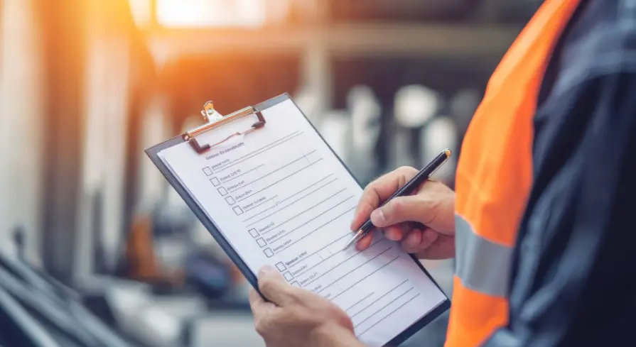 Técnico de manutenção com colete refletivo preenchendo um check-list de inspeção em prancheta, com compressores desfocados ao fundo.