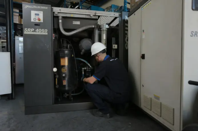 Técnico realizando inspeção em compressor de ar industrial para verificar superaquecimento e condições de operação do sistema de ar comprimido.