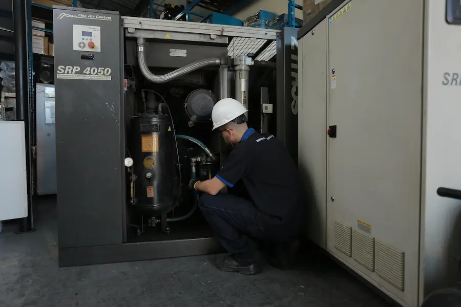 Técnico realizando inspeção em compressor de parafuso industrial para identificar falhas e perda de pressão no sistema de ar comprimido.