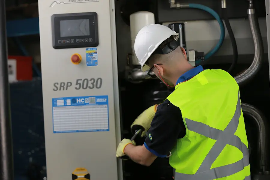 Técnico realizando manutenção em compressor de parafuso industrial, ajustando componentes internos do sistema de ar comprimido.