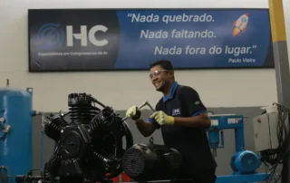 Técnico realiza manutenção em compressor de ar industrial utilizando equipamentos de proteção individual durante uma parada programada em ambiente fabril.
